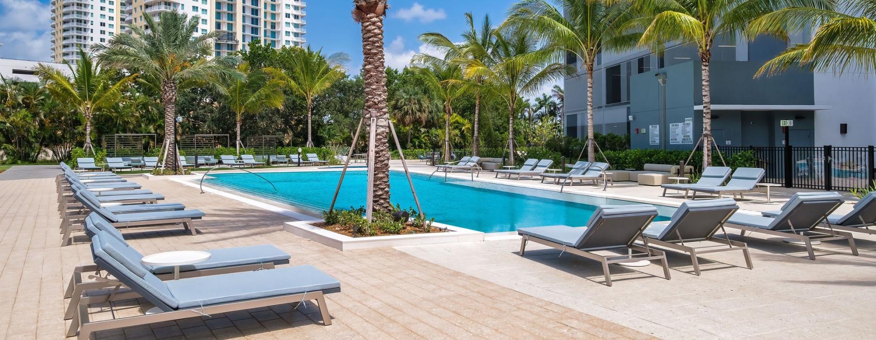 a pool with lounge chairs and palm trees by a building